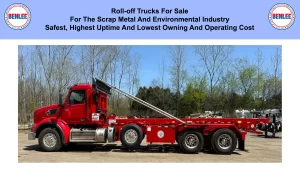 Red roll-off truck with a long flatbed trailer in an outdoor yard, set against a background of leafless trees.
